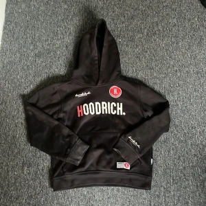Svart hoodie från Hoodrich - Säljer en svart hoodie från Hoodrich med tryck både fram och bak. Hoodien har en stor luva och långa ärmar. Perfekt för en cool och avslappnad stil. Passar åldrar 10-12 år.