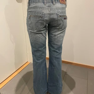 Blå jeans med bootcut - Snygga blå jeans med bootcut-stil och klassisk femficksdesign. De har en lågmidjad passform och dragkedja bak på fickorna.        Midja:36cm Innerbenslängd:72cm