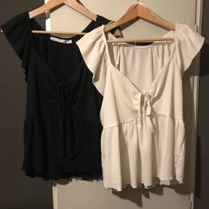 Svart och vit topp från 157 - Säljer två söta toppar från 157 i storlek L. En svart och en vit, båda med knytning framtill och volangdetaljer vid ärmarna. (den vita är använd mer än den svarta men båda i bra skick)