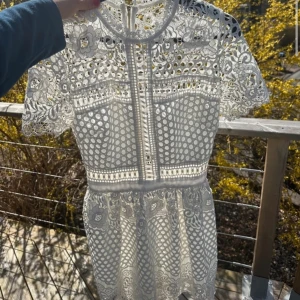 Vit spetsklänning med korta ärmar - Säljer en elegant vit spetsklänning med korta ärmar och vackra detaljer. Klänningen har ett genombrutet mönster och en figurnära passform. Perfekt för studenten! 🌸