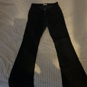 Svarta bootcut jeans Lågmidjade  - Snygga svarta bootcut jeans Lågmidjade  med klassisk femficksdesign. Perfekta för en stilren look. De har en knapp och dragkedja framtill.