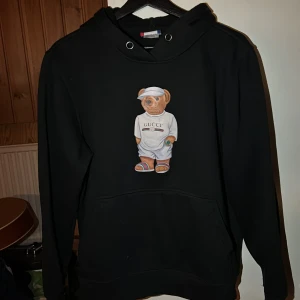 Svart hoodie med björntryck från Clique - Säljer en svart hoodie från Clique med ett coolt björntryck på framsidan. Tröjan har långa ärmar och en klassisk huva med dragsko. Perfekt för en avslappnad stil.