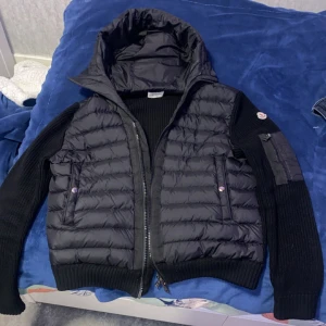 Svart cardigan  från Moncler - Säljer en snygg svart cardigan  från Moncler med quiltad design och huva. Jackan har långa ärmar och dragkedja framtill. Perfekt för kyligare dagar med sin kombination av stil och funktionalitet.