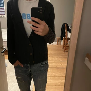 Mörkblå ribbad kofta från Raw - Säljer en snygg mörkblå kofta från g-star raw med ribbad design och knappar framtill. Koftan har en liten broderad logga på bröstet och långa ärmar. Perfekt för kyligare dagar!