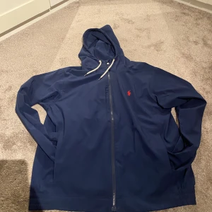 Mörkblå vindjacka från Ralph lauren  - Säljer en stilren mörkblå typ vindjacka från Ralph lauren. Perfekt för en avslappnad look. Den har långa ärmar och en enkel design som passar till det mesta. Säljer för den inte kommer till användning. Hör av dig vid intresse! 