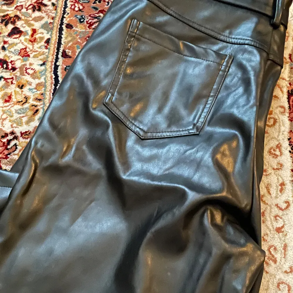Snygga svarta skinnbyxor med en stilren design. Byxorna har en rak passform och är perfekta för en trendig look. De har fickor bak och en slät yta som ger en cool känsla.. Farkut & Housut.