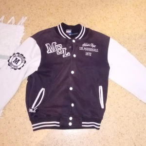 Svart och vit kofta från US Marshall - Säljer en snygg svart och vit bomberjacka från US Marshall med broderade detaljer och tryck. Jackan har vita ärmar och svarta muddar med ränder. Anledningen till varför jag säljer den är för att den var för liten. Har bara använt den 2 gånger, och det är anledning till varför den är sönder under fickan åt höger, men det funkar att fixa den med symaskin. När du köper den kan frakta den idag.