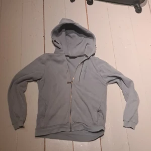 Ljusblå hoodie från Sail Racing - Säljer en stilren blå hoodie från Sail Racing. Tröjan har en dragkedja framtill och en praktisk huva. Perfekt för kyliga dagar och avslappnade stunder. Passar både till vardags och fritid. Inga fläckar och vi har hund och katt hemma