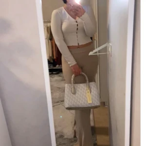 Beige handväska med mönster - Snygg beige handväska med ett diskret mönster och två handtag. Perfekt för att bära dina dagliga nödvändigheter med stil. Väskan har en elegant design som passar till många olika outfits.