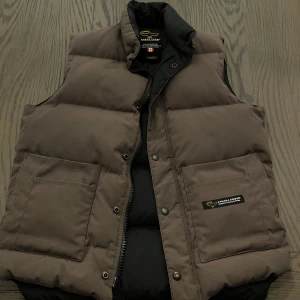 Brun dunväst från Canada Goose - Säljer en äkta Canada Goose väst. Säljer för att jag aldrig använder den. Den är i jätte bra skick. Köpt för 1700kr mitt pris 800kr.