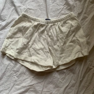 Vita brandy melville pointelle shorts - Säljer ett par vita shorts med elastisk midja. De har en avslappnad passform och är perfekta för varma dagar. Materialet ser ut att vara bekvämt och luftigt. Jättesköna pointelle!