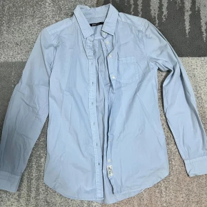 Ljusblå skjorta från Zara - Snygg ljusblå skjorta från Zara med klassisk krage och knappar framtill. Skjortan har en bröstficka och långa ärmar, perfekt för en stilren look. Passar bra till både jeans och chinos.