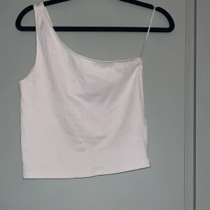 Vit oneshoulder topp från Gina Tricot - Säljer en stilren vit oneshoulder topp från Gina Tricot. Toppen är ribbad och har en smal axelrem på ena sidan. Perfekt för fest eller till vardags!