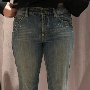 Blå jeans med broderade detaljer - Snygga blå jeans med broderade detaljer och pärlor vid fickorna. De har en bootcut-stil och är högmidjade för en bekväm passform. Perfekta för en avslappnad look med en twist.