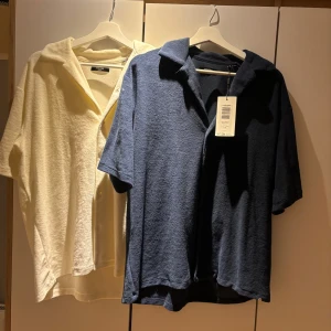 Kortärmad skjorta i frotté - Två snygga kortärmade skjortor i frotté. En i krämvit och en i marinblå. De har en avslappnad passform med knappar framtill och en klassisk krage. Perfekt för en stilren och bekväm look.                            1 st för 150kr - 2 st för 250 båda är helt oanvända och den blåa har prislapp kvar.