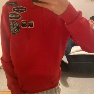 Röd hoodie från Mercier - Snygg röd hoodie från Mercier med flera coola patches på bröstet. Den har en klassisk design med huva och långa ärmar. Perfekt för en avslappnad stil.