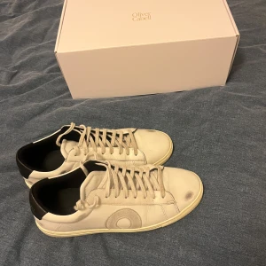 Vita sneakers från Oliver Cabell - Säljer ett par vita sneakers från Oliver Cabell med svart häl och snörning. Skorna har en stilren design med en rund tå och är tillverkade i skinn. Perfekta för en avslappnad stil. Kan även byta min något om ni har bra förslag priset är diskuterbart, snabb frakt utlovas😀