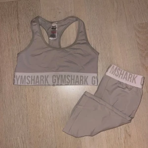 Beige sportset från Gymshark - Säljer ett snyggt beige sportset från Gymshark. Setet består av en sport-bh och matchande shorts, båda med breda resårband med Gymshark-logga. Perfekt för träning. Bh:n är i M och shortsen i S. 250kr för båda. 
