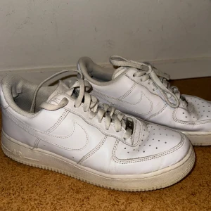 Vita Nike Air Force sneakers - Säljer ett par klassiska vita Nike Air Force sneakers. Skorna har en stilren design med snörning och perforerade detaljer på ovansidan för ventilation. Perfekta för en casual look. Lägg pris förslag!!