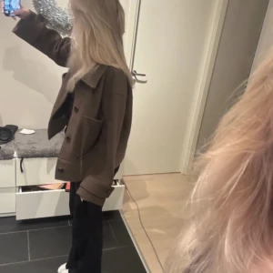 Brun kappa - Säljer en snygg brun kappa med knappar framtill. Jackan har en klassisk krage och långa ärmar. Perfekt för höst och vår. Passar bra för en stilren look.