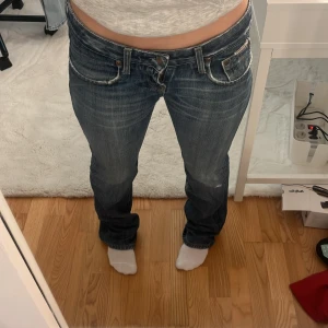 Blå bootcut jeans - Snygga blå bootcut jeans med låg midja och klassisk femficksdesign. Jeansen har en lätt slitning för en avslappnad look och stängs med dragkedja och knapp. Perfekta för en casual stil. Litet hål mellan benen som man inte ser. 