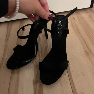 Svarta klackskor från Divided - Snygga svarta klackskor från Divided i storlek 40. De har en elegant design med smala remmar och en liten rosett framtill. Perfekta för festliga tillfällen! Skorna är i bra skick och redo att användas. Passar 39 lika bra. Aldrig använda bara stått och dammat (fixar såklart vid försäljning). Inte fri frakt.