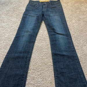 Mörkblå jeans med broderade bakfickor - Säljer dessa snygga par mörkblå jeans i bra skick. De har en en skitsnygg design på fickorna fram och coola broderade detaljer på bakfickorna. Jeansen är lågmidjade och har en rak/bootcut passform och är perfekta för både vardag och fest. 