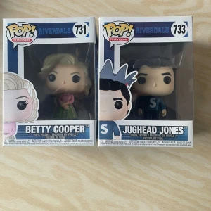 Funko Pop! Riverdale Betty Cooper och Jughead Jones - Säljer två coola Funko Pop! figurer från Riverdale-serien. Betty Cooper (#731) har en söt rosa topp och grön kjol, medan Jughead Jones (#733) har sin ikoniska krona och blå tröja med 'S'. Perfekta för samlare eller Riverdale-fans! Figurerna är i originalförpackning. Köpta för 300kr var men säljer en för 100kr eller båda tillsammans för 170kr!
