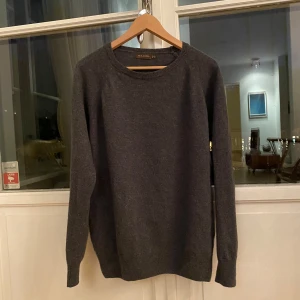 Mörkgrå ulltröja från Oscar Jacobson - Säljer en stilren mörkgrå tröja från Oscar Jacobson i storlek L. Den är tillverkad i Italien och består av 80% ull och 20% nylon, vilket gör den både varm och bekväm. Perfekt för höst och vinter! Tröjan har en rund hals och långa ärmar. Använd skonsamt tvättprogram för att bevara kvaliteten.
