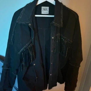 Svart jacka med glitter från Zara - Säljer en svart jacka från Zara i storlek M. Den har snygga glitter fransdetaljer på både fram- och baksidan. Skickar gärna mer bilder vid intresse!