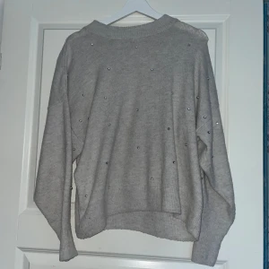 Grå tröja med pärlor från H&M - Säljer en superfin grå tröja från H&M i storlek M. Den är dekorerad med små pärlor som ger en extra touch. Perfekt för både vardag och fest! Tröjan är i bra skick och har långa ärmar. Passar perfekt till höst och vinter. Jätteskön!