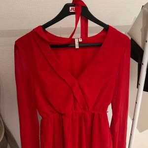 Röd blus med v-ringning och knytning - Snygg röd blus med v-ringning och långa ärmar. Perfekt för festliga tillfällen. Den har en smickrande passform med ett band i midjan som ger en fin siluett. Materialet känns mjukt och bekvämt mot huden.
