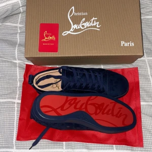 Mörkblå sneakers från Christian Louboutin - Säljer ett par snygga mörkblå sneakers från Christian Louboutin. Skorna är i mocka och har den ikoniska röda sulan. De kommer med originalkartong och röd dustbag. Perfekta för att ge din outfit en lyxig touch! OBS PRIS EJ HUGGET I STEN 