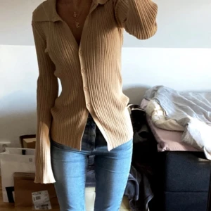 Beige ribbad kofta - Säljer en superfin beige ribbad kofta med knappar hela vägen ner. Den är perfekt för höst och vår, och har en snygg v-ringad design. Koftan är i mycket bra skick och passar perfekt till jeans för en avslappnad look.