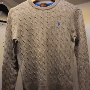 Beige kabelstickad tröja från Morris - Säljer en snygg beige kabelstickad tröja från Morris i 100% merinoull. Den har en liten blå broderad logga på bröstet och är perfekt för både höst och vinter. Tröjan är i mycket bra skick och har långa ärmar med ribbade muddar. Perfekt för en stilren och varm look!