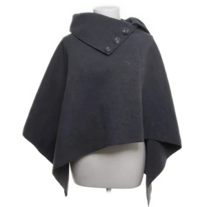 Grå poncho från Luigi - Säljer en stilren grå poncho från Luigi i ull och viskos. Den har en asymmetrisk design med knappar vid halsen för en elegant touch. Perfekt för höst och vår när du vill hålla dig varm och snygg. Passar till alla tillfällen!