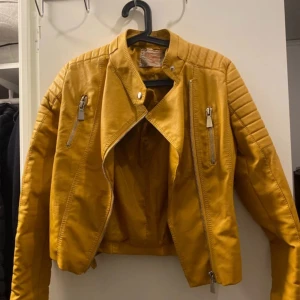 Gul skinnjacka från Vogelle - Säljer en snygg gul skinnjacka från Vogelle i storlek 38. Jackan har en cool bikerstil med dragkedjor och knappar. Perfekt för höst och vår, och den ger en färgklick till vilken outfit som helst. Jackan är i mycket bra skick och redo för nya äventyr! 💛