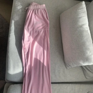Rosa mjukisbyxor från Juicy Couture - Supermysiga rosa mjukisbyxor från Juicy Couture i storlek 14/15. De är gjorda i ett mjukt material och har en elastisk midja för extra komfort. Byxorna har en snygg broderad logga och fickor med knappar. Perfekta för en chill dag hemma eller en avslappnad utflykt! 💖