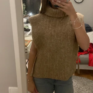 Beige stickad ärmlös tröja - Den har en hög krage som håller dig varm och är i ett löst passande snitt. Jätte mysig! 