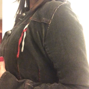 Mörkgrå manchesterjacka med knappar - Säljer en mörkgrå jacka i bra skick med stora knappar framtill. Den har långa ärmar och en cool detalj med röda och vita snören på bröstet. Perfekt för höst och vår, och funkar både till vardags och fest. Passar bra till jeans eller klänning! På bilden ser jackan liten ut och det beror på att jag är idag en stl 40/42 och jackan är i stl 36