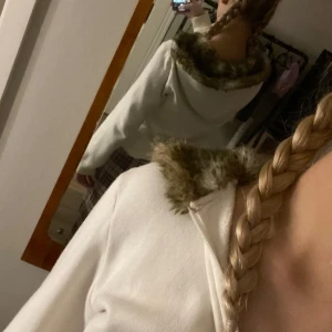 Vit hoodie med päls - Mysig vit hoodie med dragkedja och fuskpäls i luvan. Perfekt för kyliga dagar när du vill vara både varm och stilren. Den har en normal passform och är gjord i mjukt material. Två fickor framtill för extra bekvämlighet.