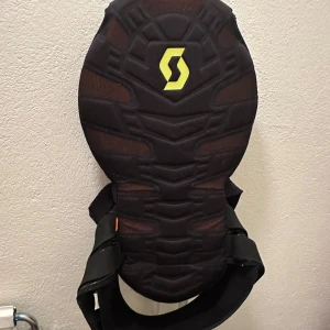 Svart skyddsväst från Scott - Säljer en svart ryggskydd från Scott i storlek XL. Västen har en robust design med vaddering för extra skydd. Perfekt för aktiviteter som kräver extra säkerhet. Den är i mycket bra skick och redo för nya äventyr!
