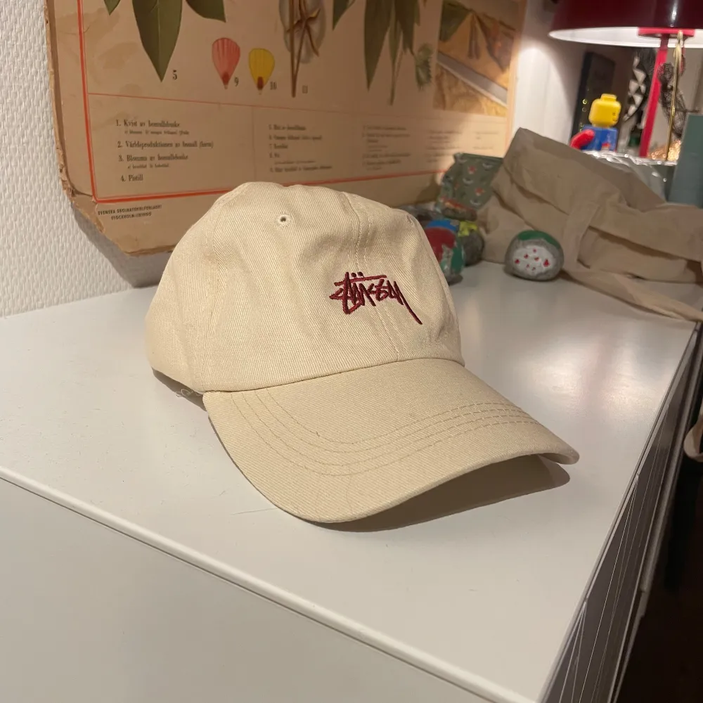 Säljer en snygg beige keps från Stüssy i mycket bra skick. Den har en broderad logga i rött framtill och justerbar rem bak.. Accessoarer.