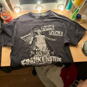 Cool svart t-shirt från H&M med ett retro Bride of Frankenstein-tryck. Perfekt för dig som gillar klassiska skräckfilmer! T-shirten är kortärmad och i bomull, vilket gör den skön att ha på sig. Passar perfekt till vardags eller en avslappnad festkväll!🖤