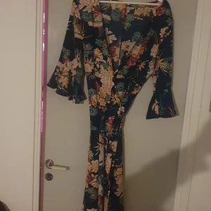 Blommig långklänning med volangärmar - Säljer en superfin omlottskllänning med blommigt mönster i härliga färger. Klänningen har volangärmar och en omlott-design som ger en snygg passform. Perfekt för sommarens fester eller en mysig vårdag. Materialet känns lätt och luftigt.
