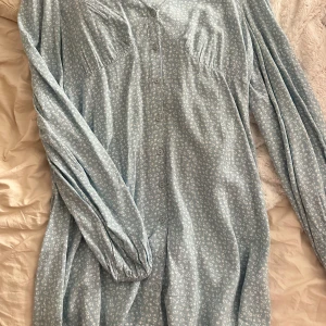 Ljusblå blommig klänning från Nelly - Säljer en superfin ljusblå klänning från Nelly med små vita blommor. Den har en v-ringad hals och knappar framtill. Perfekt för vår och sommar! 💙