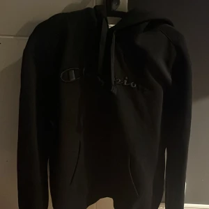 Svart hoodie från Champion - Säljer en svart hoodie från Champion i storlek L. Den är i nyskick och helt oanvänd. Hoodien har en klassisk design med en stor ficka framtill. 