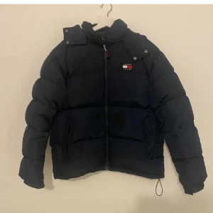Mörkblå Alaska pufferjacka från Tommy Hilfiger - Säljer en mörkblå svart pufferjacka från Tommy Hilfiger. Den är perfekt för kalla dagar med sin tjocka vaddering och är i 10/10 skick. Den passar perfekt nu och är redo för vintern! ❄️.          Orginal pris 3000kr