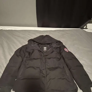 Svart dunjacka från Canada Goose - Säljer en svart dunjacka från Canada Goose i mycket bra skick. Jackan är perfekt för kalla vinterdagar och har en klassisk design med långärmade ärmar och dragkedja. Den är varm och stilren, perfekt för både vardag och fest. Storleken är dam M.