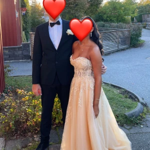 Gul  axelbandslös balklänning - Säljer en fantastisk champagnefärgad balklänning i axelbandslös design. Klänningen har en vacker spetsdetalj på överdelen och en lång, flödande kjol. Perfekt för bal eller fest! 💃✨